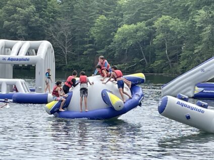 Campers playing on an inflatable toy in the lake in summer.